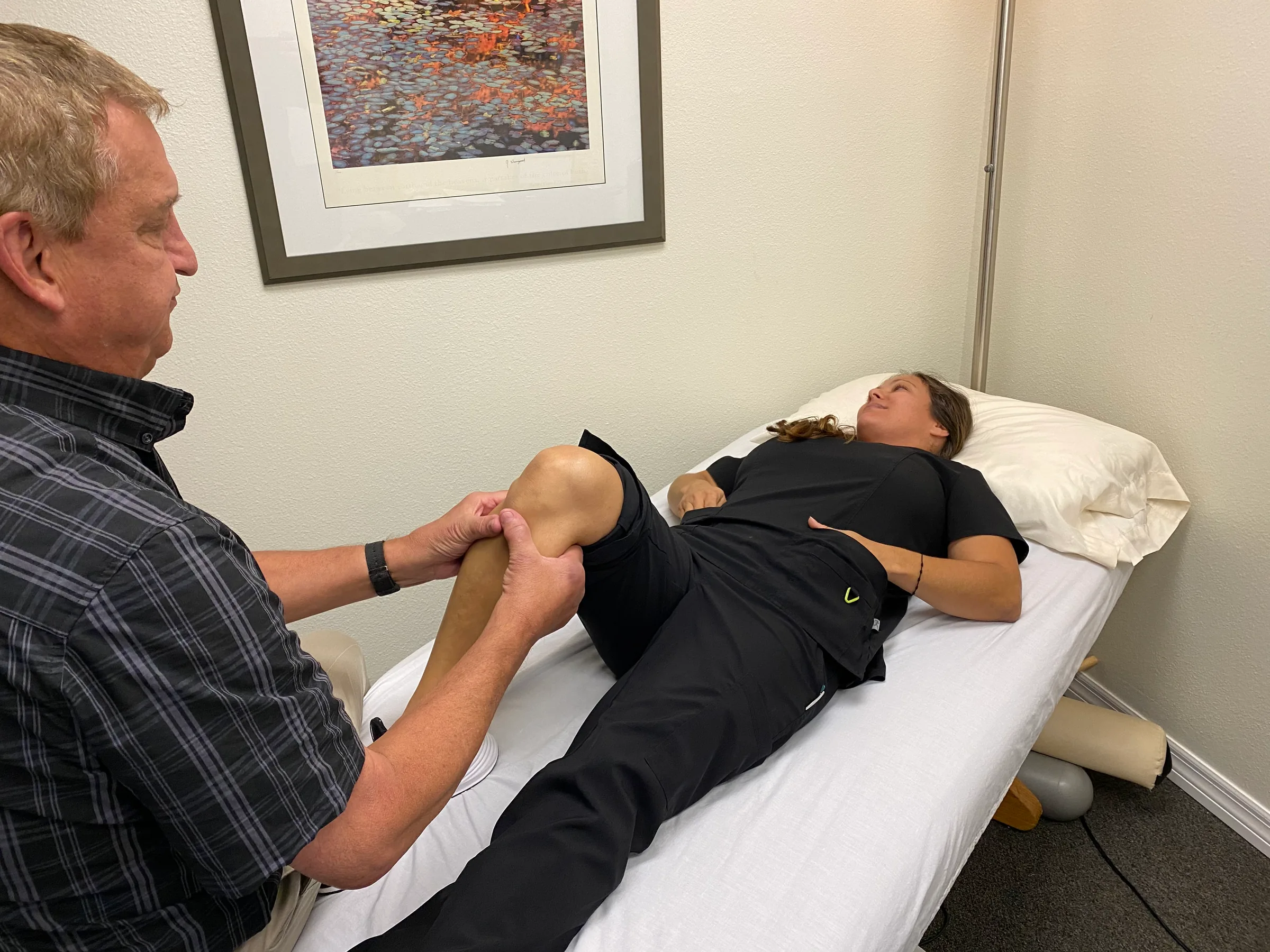 Chiropractor performing knee examination on patient lying on treatment table.